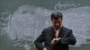 Former Iranian President Mahmud Ahmadinejad looks at his watch in front of the chalkboard in a university lecture hall. (file photo)