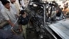 A policeman and residents gather near a damaged car at the site of the bomb blast near a religious school in Peshawar on May 24.