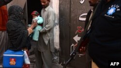 A Pakistani policeman stands guard as a polio-vaccination worker marks a child after immunization with antipolio drops in Lahore on December 21.