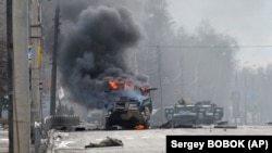 Російський бронетранспортер (БТР) горить біля тіла невпізнаного солдата під час бою з бійцями Збройних сил України на околиці Харкова. Після вуличних боїв ЗСУ відновили повний контроль на Харковом. Фото від 27 лютого 2022 року